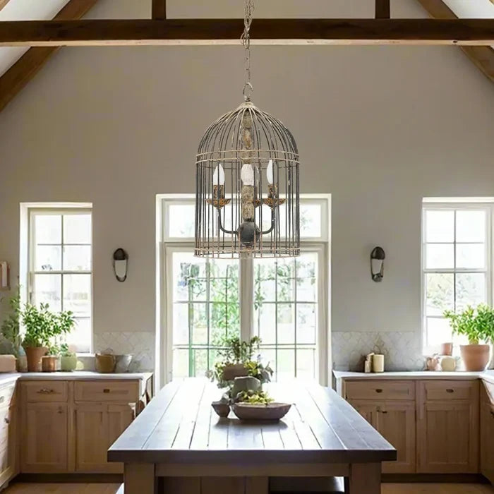 Rustic metal bird cage pendant lamp with distressed finish and candelabra bulb holders, hanging by chain in farmhouse kitchen dining