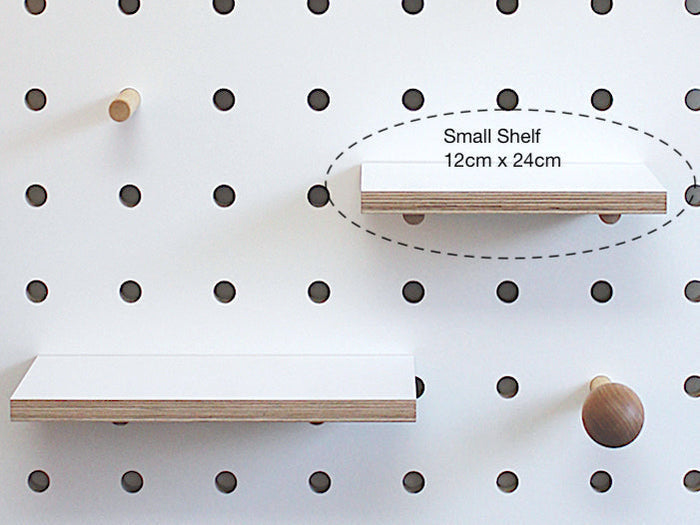 Small wood shelf in white plywood shown on white pegboard. Shelf is fitted with pegs to slot into pegboard. Made by Kreisdesign in UK