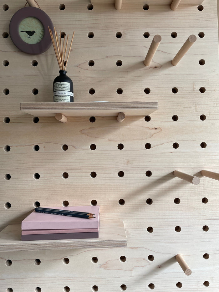 detail of shelves and pegs with accessories of a maple veneer plywood pegboard by kreisdesign. books and a round picture frame hanging off a beech peg