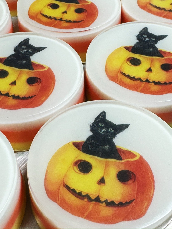 Round white soaps decorated with a Halloween design featuring a black cat sitting inside a carved orange pumpkin.