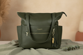 Lillian diaper bag in Palmetto green vegan leather on warm earthy sage linen surface with eucalyptus