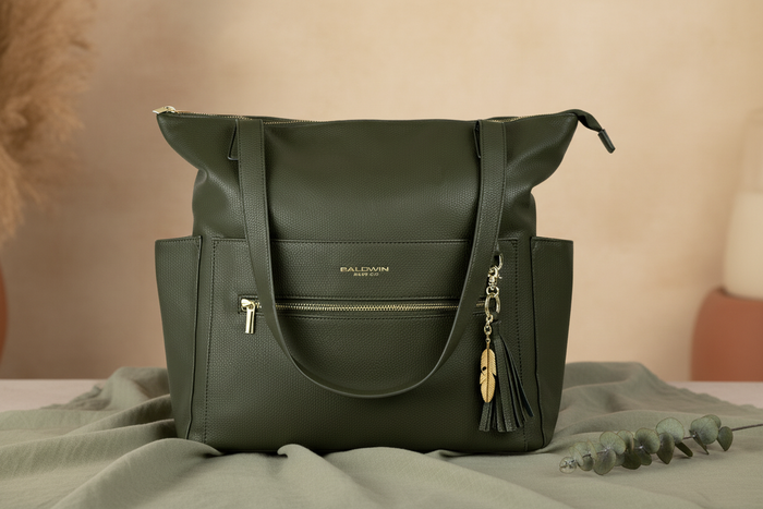 Lillian diaper bag in Palmetto green vegan leather on warm earthy sage linen surface with eucalyptus
