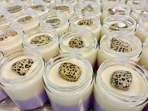 Multiple small clear glass jars filled with layered white and purple body butter, each topped with a tumbled dalmation jasper crystal