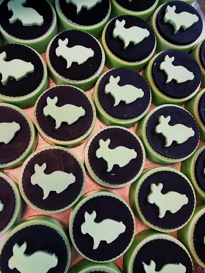 A close-up overhead view of multiple round green and black soaps arranged in rows, each topped with a pale mint bunny silhouette.